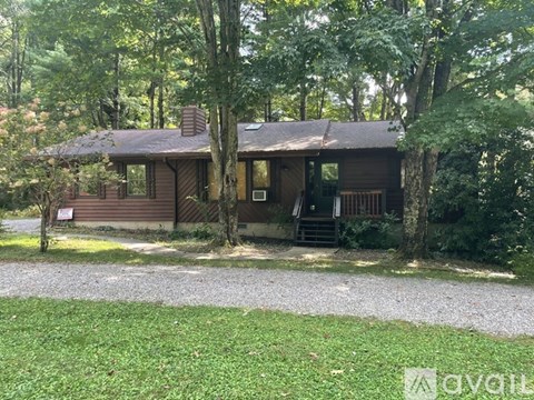 A cabin in the woods with a gravel driveway leading to it.