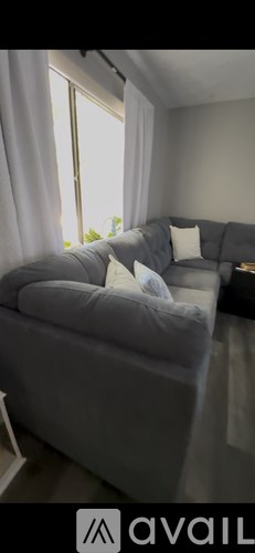 A grey couch with white pillows sits in a room with a window.