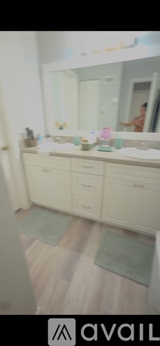 A bathroom with a mirror, sink, and a person in the background.