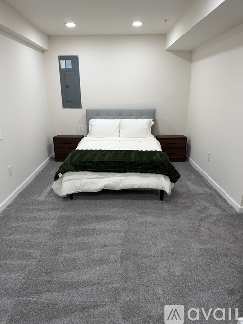 A bedroom with a bed, nightstand, and a grey carpet.