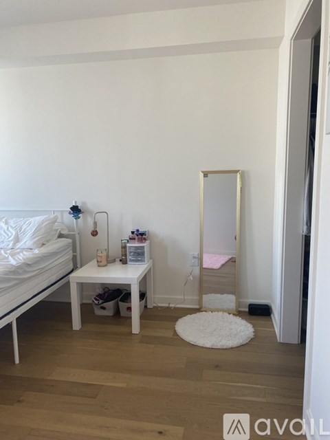 A white bedroom with a bed, a small table with a mirror and a rug on the floor.