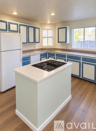 A kitchen with a white refrigerator and a white island with a black stove top.