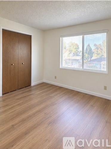 A room with a wooden floor and a window showing trees outside.