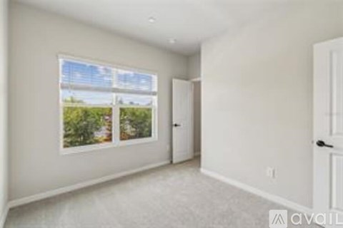A room with a window showing a view of trees and a door on the right.