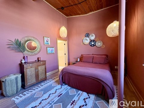 A bedroom with a pink wall and a bed with a pink blanket.