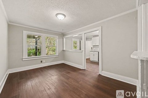 A room with wooden floors and white walls, featuring a window with a view of trees and a small white cabinet.