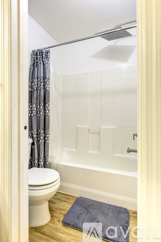 A bathroom with a toilet, a shower, and a blue towel on the floor.