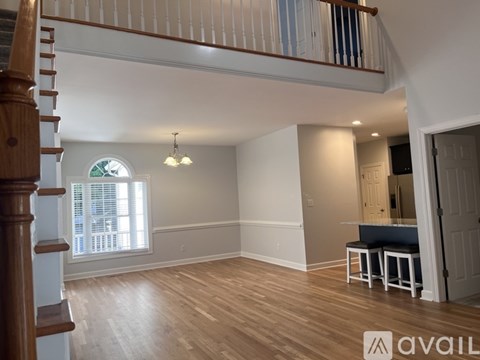 A spacious room with wooden floors and a staircase on the left side.