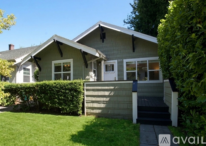A house with a grey exterior and a white door is surrounded by greenery.