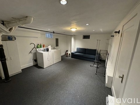 A spacious room with a grey carpet and white walls, containing a black sofa, a white cabinet, and a small table with a plant on it.