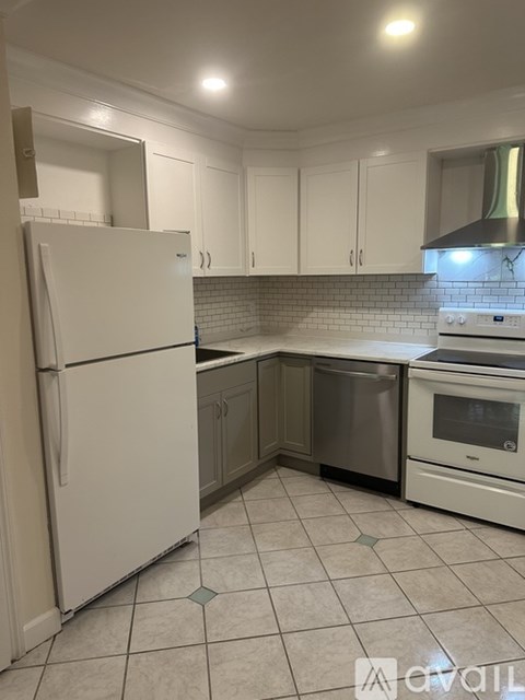 A white refrigerator stands in a kitchen with white cabinets and a white stove.