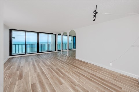 A room with wooden flooring and a balcony with a view of the ocean.