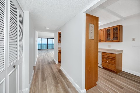 A hallway with wooden floors and white walls leading to a kitchen area.