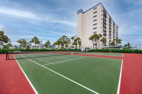 A tennis court is in front of a tall building.