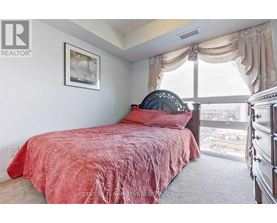 A bedroom with a red bedspread and a large window.