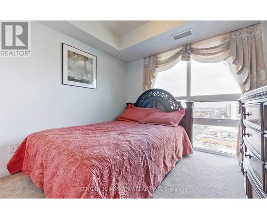 A bedroom with a red bedspread and a large window.