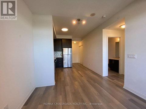 A spacious room with wooden flooring and white walls, with a trash bin and a doorway leading to another room.