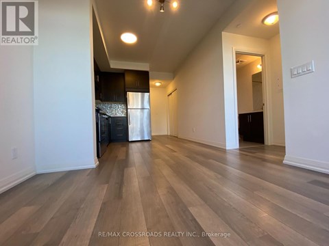 A spacious room with wooden flooring and a kitchen area in the background.
