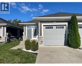 A house with a grey garage door and a green tree in front.