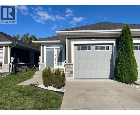 A house with a grey garage door and a green tree in front.