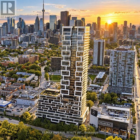 A tall, modern building stands in the foreground of a cityscape at sunset.
