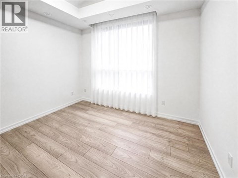 A room with wooden flooring and a window with white curtains.