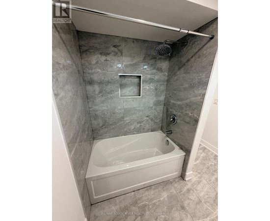 A bathroom with a white tub and grey tiled walls.