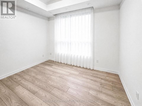 A room with wooden flooring and a window with white curtains.