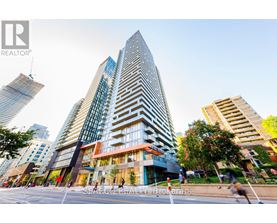 A tall building with a glass facade stands in the foreground of a city street.