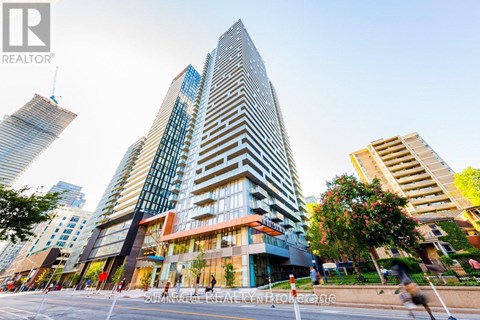 A tall building with a glass facade stands in the foreground of a city street.