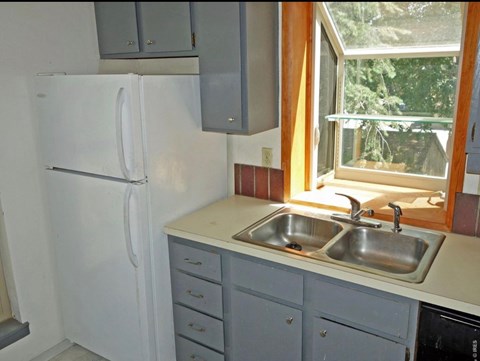 A white refrigerator is in a kitchen with a window above the sink.
