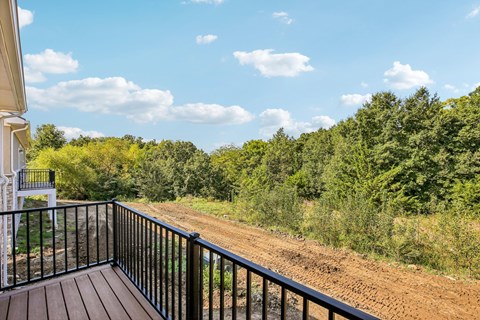 Balcony overlooks a dirt road with trees on the side.
