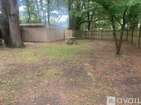 A backyard with a fence, a tree, and a picnic table.