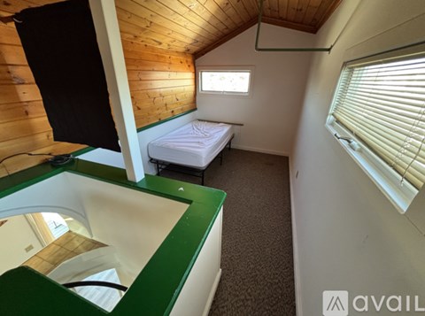 A small bedroom with a bed, window, and wooden walls.