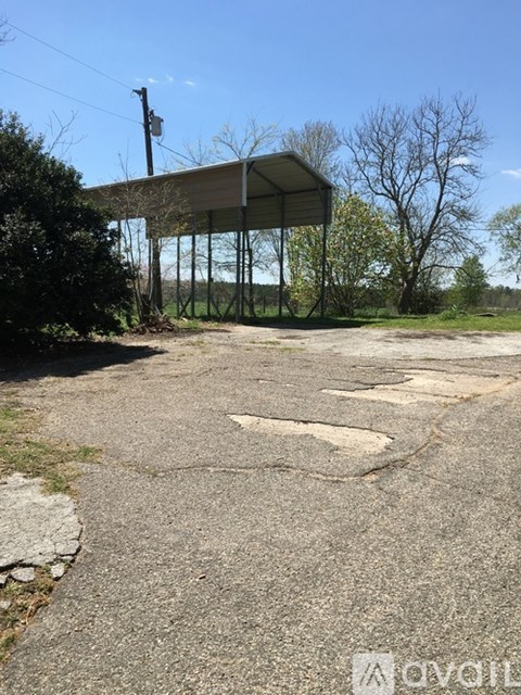 A small building with a metal roof is surrounded by a grassy area and a cracked concrete ground.