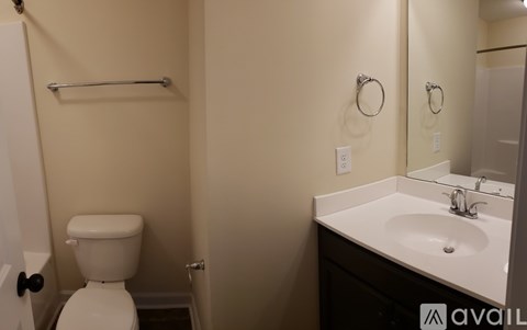 A bathroom with a toilet, sink, mirror, and towel bar.