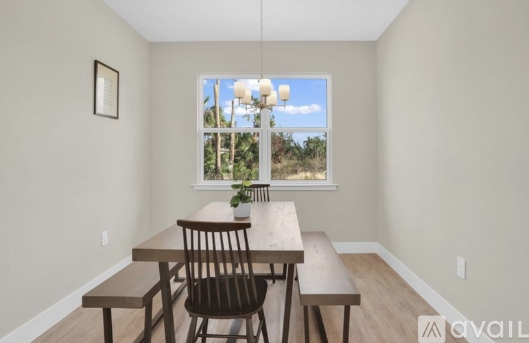 A dining room with a wooden table and bench, a window with a view of the outdoors, and a framed picture on the wall.