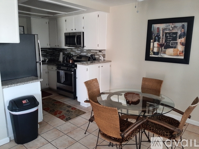 A kitchen with a black fridge, white cabinets, a glass table with four chairs, and a painting on the wall.