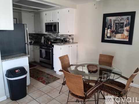 A kitchen with a black fridge, white cabinets, a glass table with four chairs, and a painting on the wall.