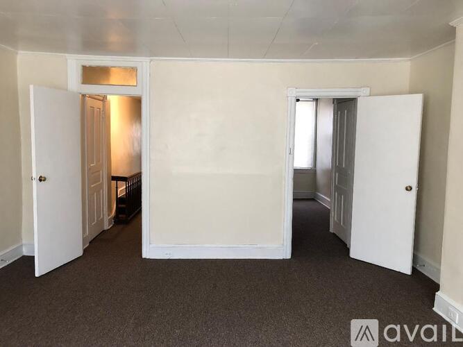 A room with carpeted floor and white walls, with two doors open.