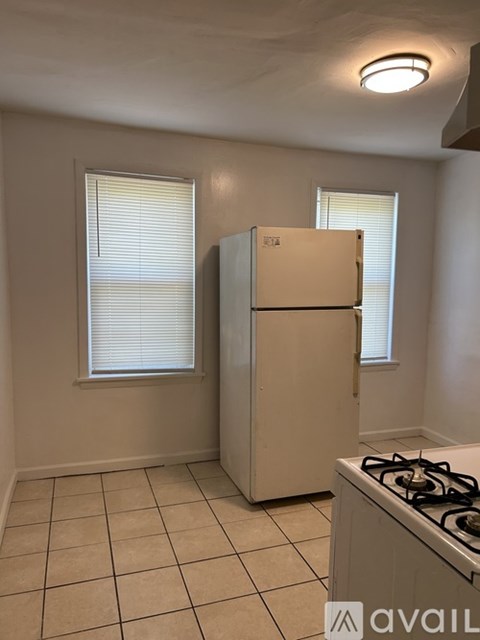 A kitchen with a beige refrigerator, a white stove, and a window with blinds.