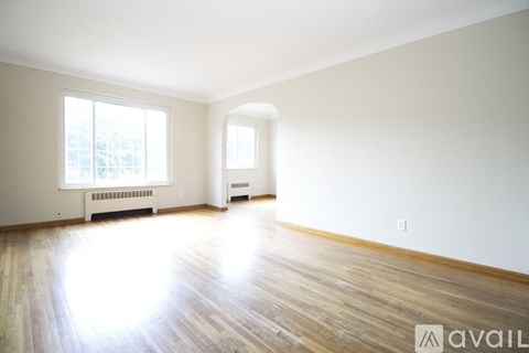 A spacious room with wooden floors and two windows.