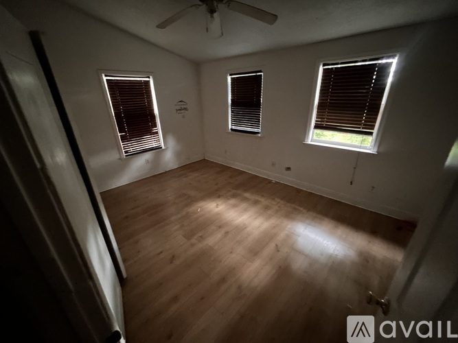A room with wooden flooring and three windows with blinds.