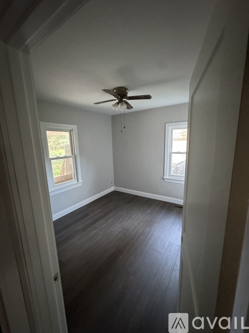 A room with a ceiling fan and two windows.
