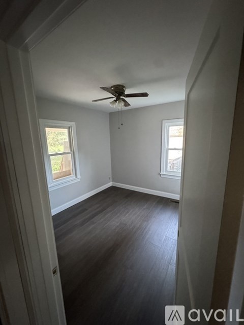 A room with a ceiling fan and two windows.