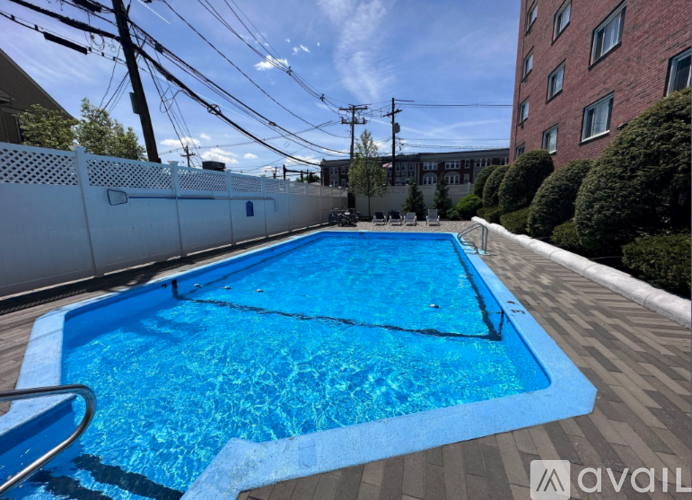 A blue swimming pool surrounded by a white fence and a brick building in the background.