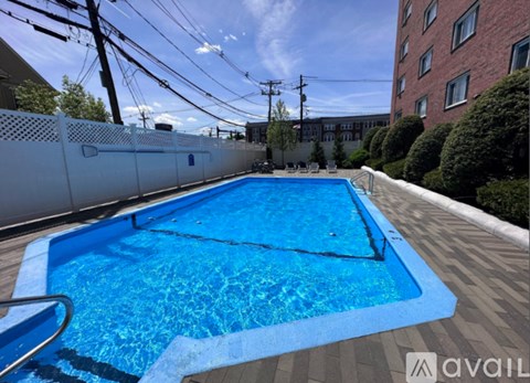 A blue swimming pool surrounded by a white fence and a brick building in the background.