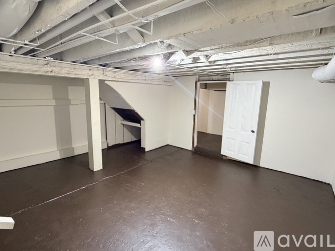 A spacious room with a concrete floor and white walls, featuring a large open doorway and a white door.