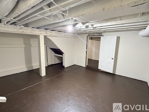 A spacious room with a concrete floor and white walls, featuring a large open doorway and a white door.