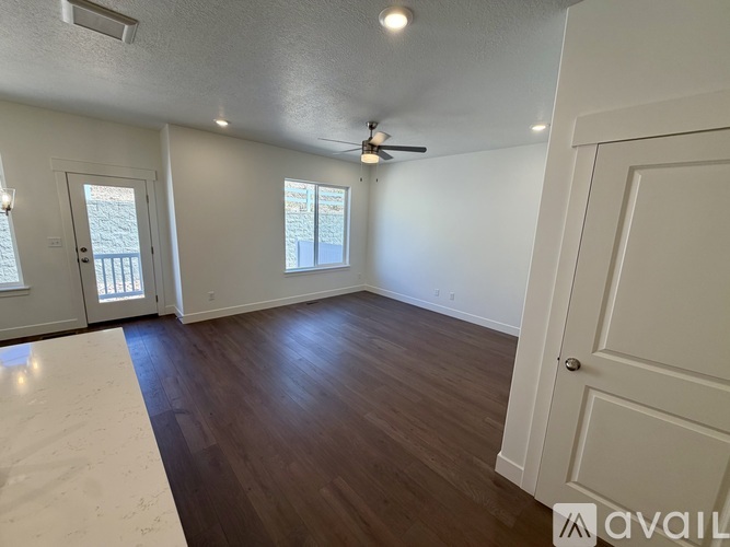 A room with wooden floors and white walls, featuring a ceiling fan and two windows.